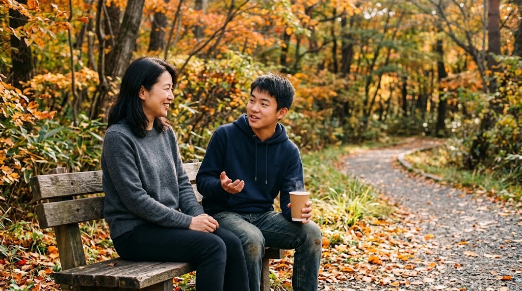 紅葉の公園のベンチで、母親と高校生の息子が並んで座り、笑顔で話している様子