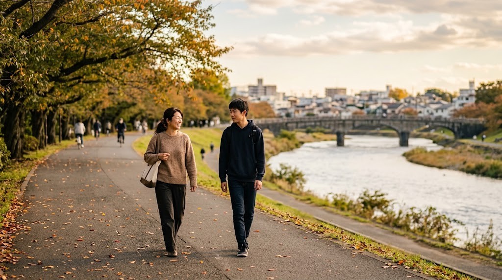 秋の川沿いの並木道を、母親と高校生の息子が並んで歩いている。奥に石の橋が見える