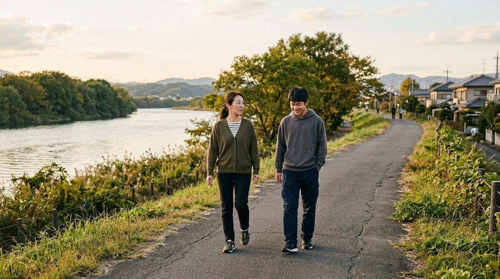 夕方の川沿いの道を、高校生と親が並んで歩きながら話している様子